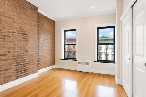 Bedroom with exposed brick wall, hardwood floors, two windows with city views, and white closet doors.