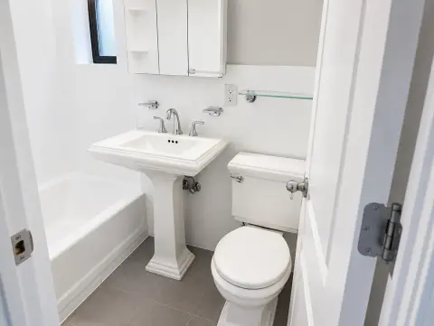 Bathroom with white pedestal sink, toilet, bathtub, mirrored medicine cabinet and tile flooring.