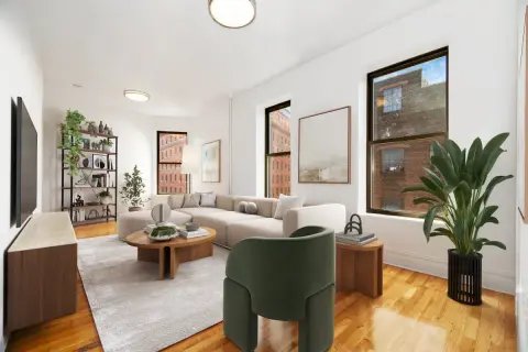 Living room with hardwood floors, large windows, beige sofa, green armchair, wooden coffee table and potted plants.