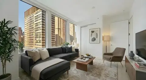 Living room with black sectional sofa, floor-to-ceiling windows overlooking city skyline, wooden coffee table, and modern furnishings.