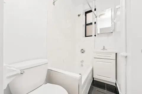 Bathroom with white walls, toilet, sink vanity, mirror, and dark tile flooring.