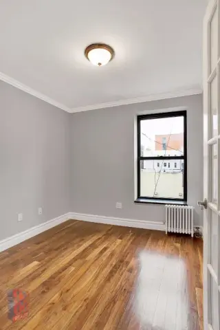Empty bedroom with lavender walls, hardwood floors, ceiling light fixture, and a window with black frame.