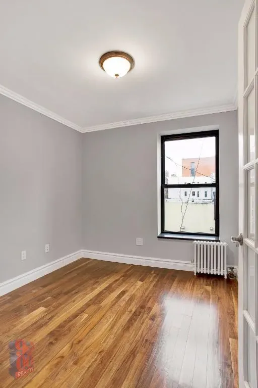 Empty bedroom with lavender walls, hardwood floors, ceiling light fixture, and a window with black frame.