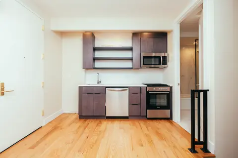 Kitchen with brown cabinetry, stainless steel appliances, open shelving, and hardwood floors.