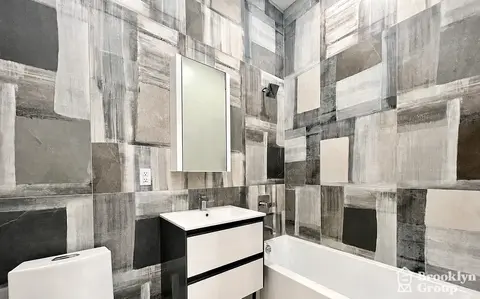 Bathroom with geometric tile walls, white sink vanity with black drawers, toilet, and bathtub.