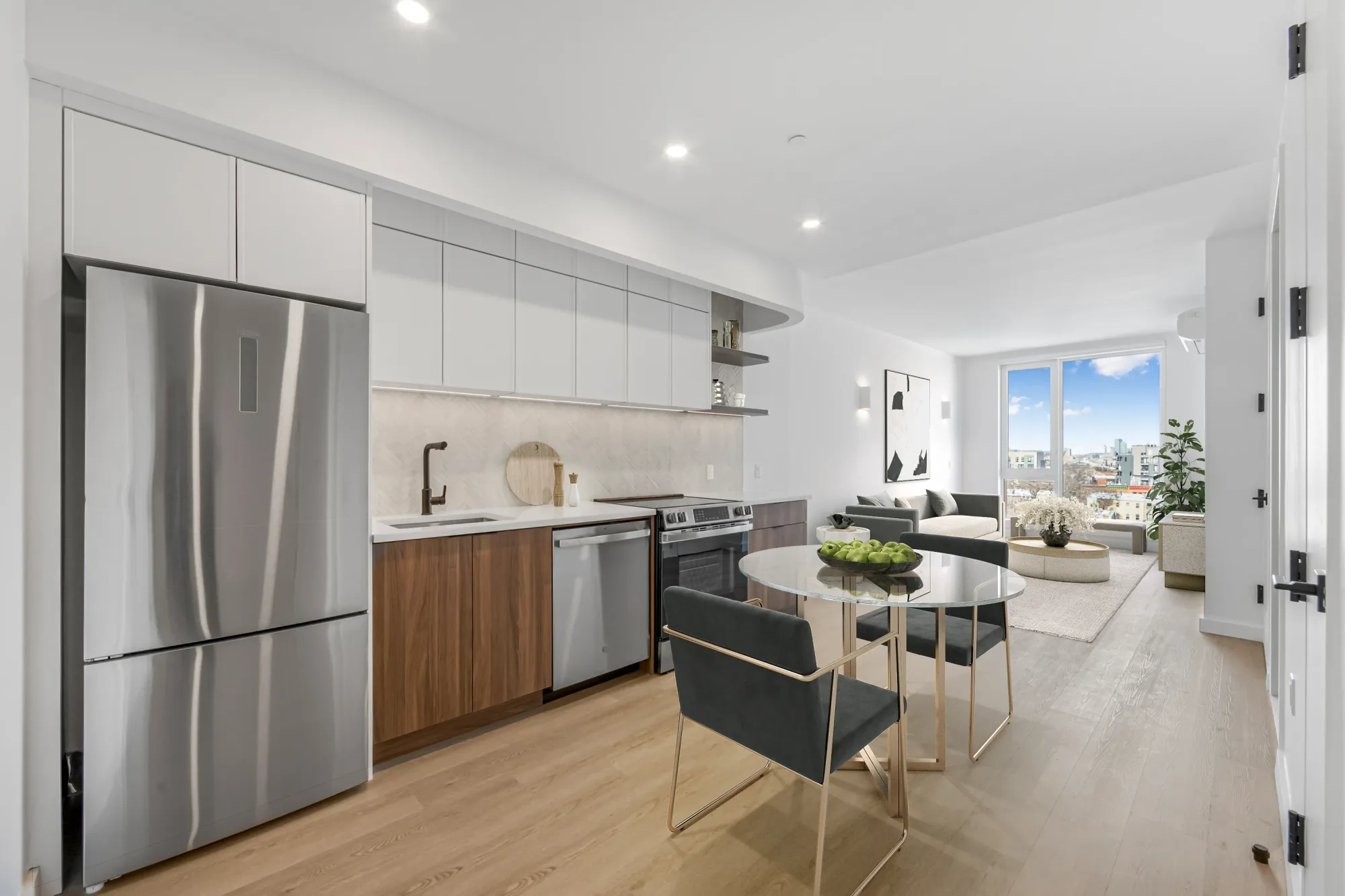 Modern kitchen with stainless steel appliances, white cabinetry, wood accents, dining table, and city views through large windows.