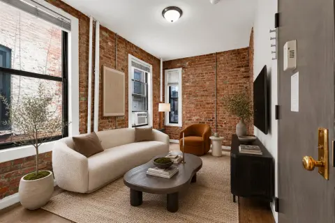 Living room with exposed brick walls, cream curved sofa, black coffee table, large windows and hardwood floors.
