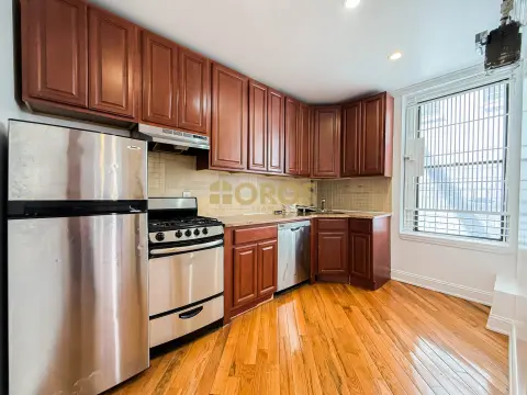 Kitchen with red wood cabinets, stainless steel appliances, tile backsplash, hardwood floors and window with blinds.