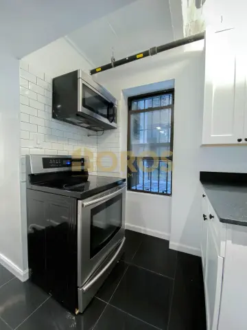 Kitchen with white subway tile backsplash, black countertops, stainless steel appliances, and dark tile flooring.