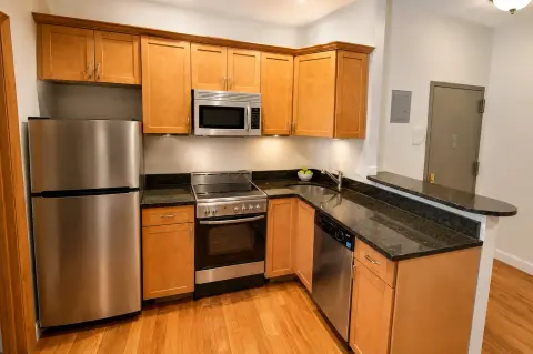 Kitchen with wooden cabinets, stainless steel appliances, black countertops, and hardwood floors.
