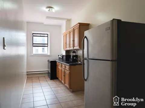 Kitchen with tile flooring, wooden cabinets, stainless steel refrigerator, and a window with blinds.