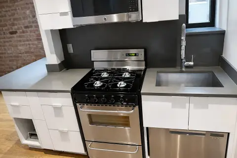 Kitchen with white cabinets, black gas range, stainless steel sink and appliances, dark backsplash, and brick accent wall.