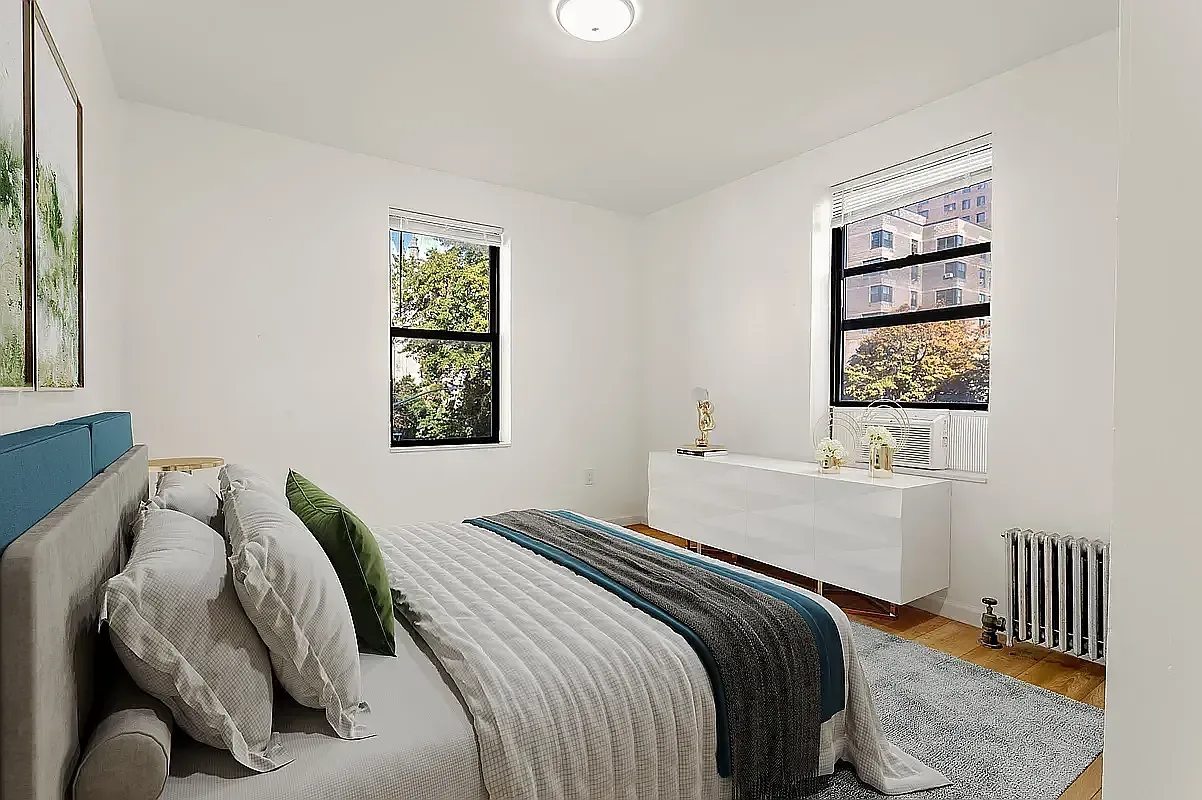 Bedroom with queen bed, two windows, white dresser, hardwood floors, and radiator heating.