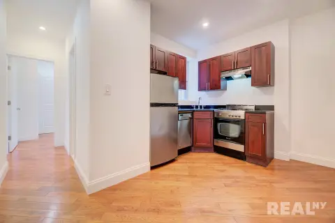 Kitchen with red wood cabinets, stainless steel appliances, black countertop, and hardwood floors.