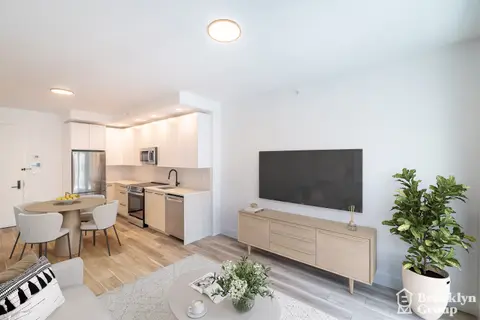Open-plan living room and kitchen with wooden floors, white walls, dining table, TV unit, and potted plants.