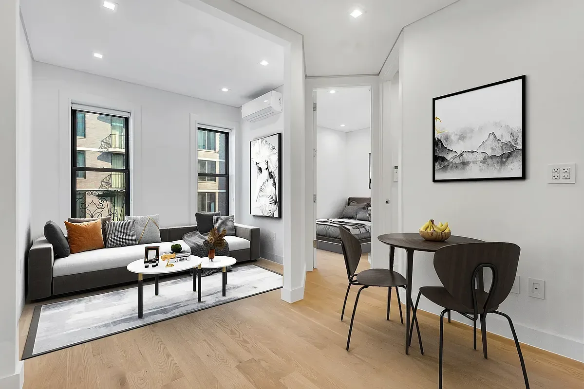 Open-plan living and dining area with light wood floors, white walls, built-in shelving, sofa, dining table and chairs.