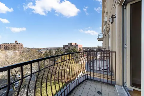 Balcony with black metal railing overlooking cityscape, blue sky, and distant buildings.