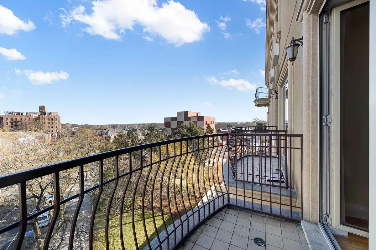Balcony with black metal railing overlooking cityscape, blue sky, and distant buildings.
