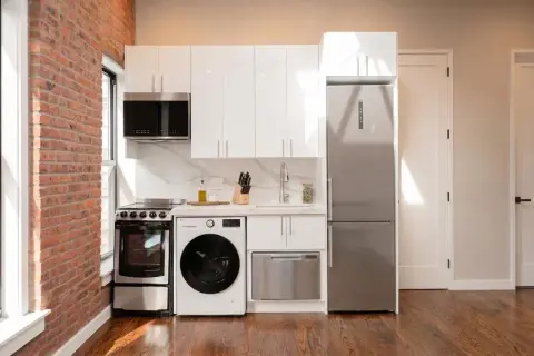 Kitchen with white cabinetry, stainless steel appliances, exposed brick wall, and hardwood floors.